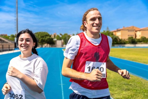 Two happy athletes running a race on a blue track at an athletics stadium under a clear blue sky