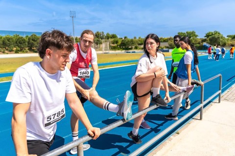 Runners stretching their legs on a railing, preparing for competition on an athletics track under a