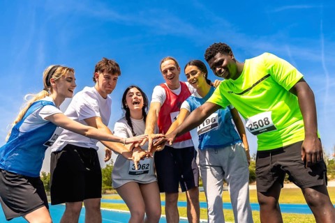 Diverse group of young athletes putting their hands together before a track and field competition,