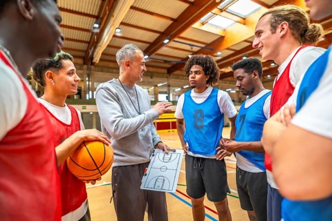 Basketball coach discussing game strategy with team members while using a clipboard on the
