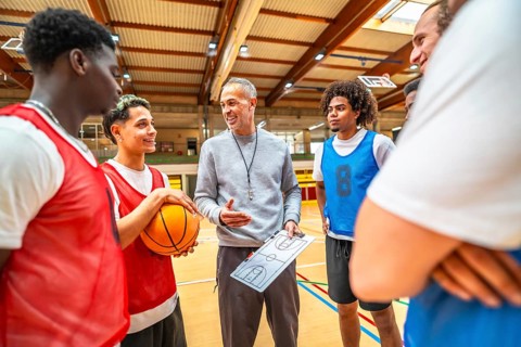 Basketball coach explaining game strategy to a multi ethnic team using a clipboard in a gymnasium,