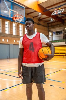 Young male basketball player holding a ball while standing confidently on a polished wooden court
