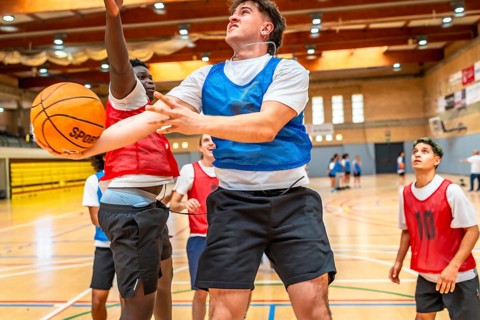 Two basketball players jumping for a rebound during a fast paced indoor court game, showcasing