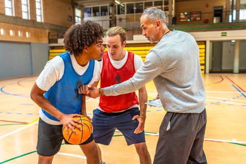 Basketball coach holding clipboard explaining game strategy to two players practicing during