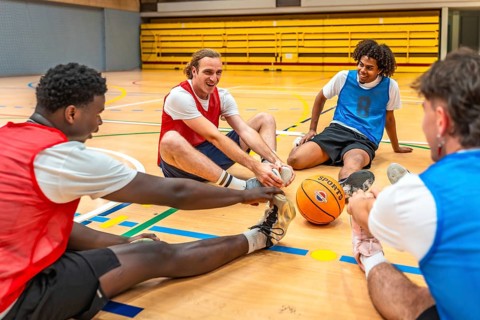 Four happy basketball players stretching their legs on the court before a game, showing teamwork