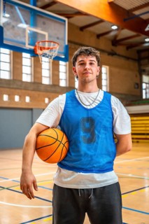 Young male basketball player holding ball in indoor court posing after training, looking confident