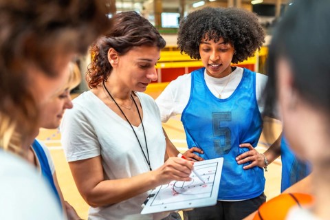 Basketball coach explaining game strategy to her team using whiteboard, during training in the