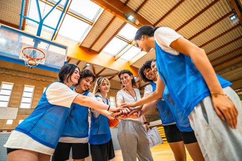 Female basketball players and their coach stacking hands, demonstrating teamwork and unity before a