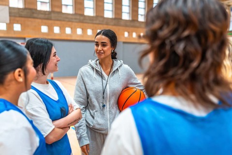 Female basketball coach holding a ball and engaging with her team during an intense training