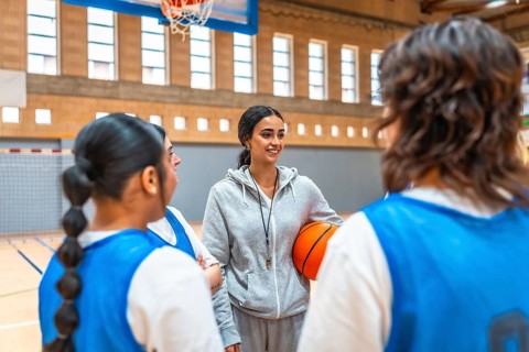 Female basketball coach holding a ball while engaging with her team during an intense training
