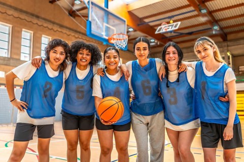 Diverse group of female basketball players hugging and holding ball, showcasing team unity and