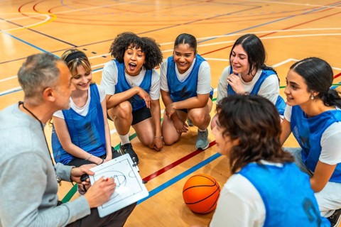 Female basketball team listening to their coach explaining game strategy on a clipboard during a