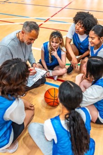 High angle view of a basketball coach drawing a play on a clipboard while sitting on the court with