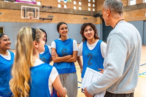 High school girls basketball team listening to their coach explain game strategy on a clipboard in