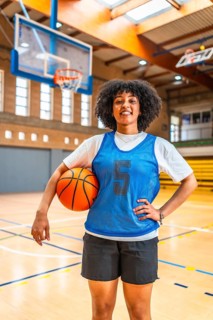 Young woman basketball player smiling while holding a ball on the court, exuding confidence and