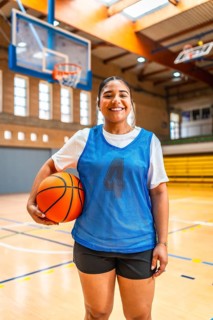 Young female athlete wearing blue jersey and black shorts, holding basketball and smiling in an