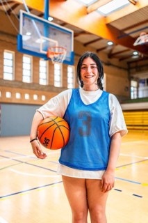 Female athlete smiling and holding basketball in a gymnasium, ready for training or competition