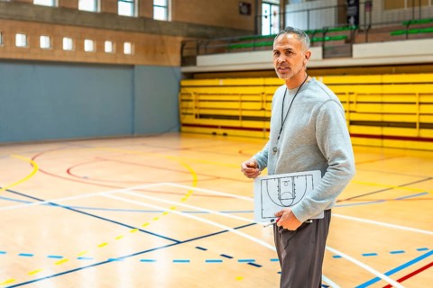 Mature basketball coach holding clipboard with game strategy explaining tactics to team players in