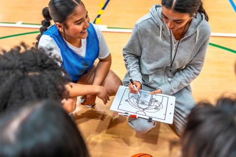 Female basketball coach drawing a play on a clipboard and explaining game strategy to her team