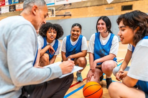 Basketball coach briefing his female team during a time out, taking notes and discussing game