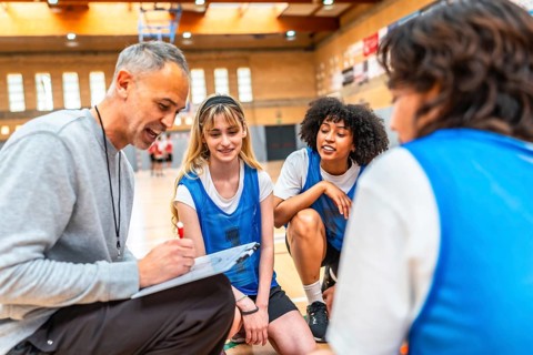 Basketball coach drawing a play on clipboard and explaining game strategy to his multi ethnic