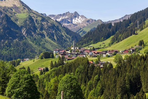 The mountain village of Mittelberg with its church nestled in a wooded valley landscape in