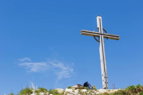 Summit cross of the Kuhgehrenspitze in Mittelberg rises in front of a bright blue sky in