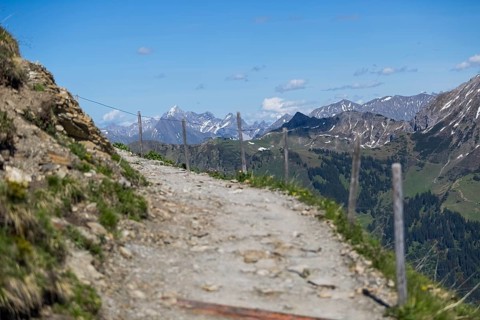 Stony hiking trail along a fence with a mountain backdrop and blue sky