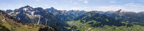 An expansive mountain panorama with green valleys under a partly cloudy sky with a view of the Hohe