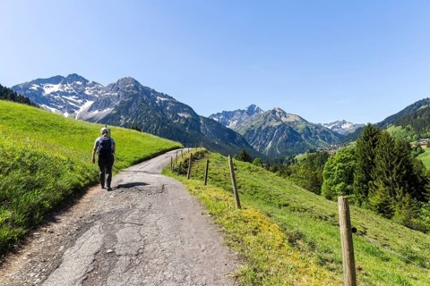 Woman walking on a path through a green hilly landscape with mountain views