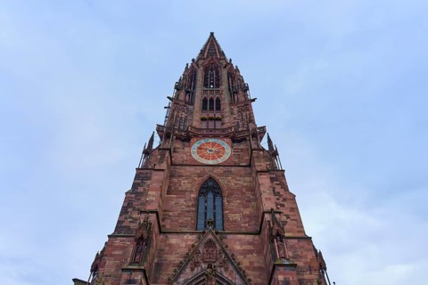 Freiburg Minster, Imposing Gothic church tower made of red stone with clock and windows, Freiburg