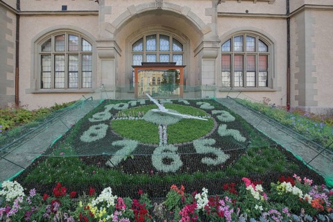 Flower clock made of blooming flower-bed with flower bed, garden art, clock face, information board