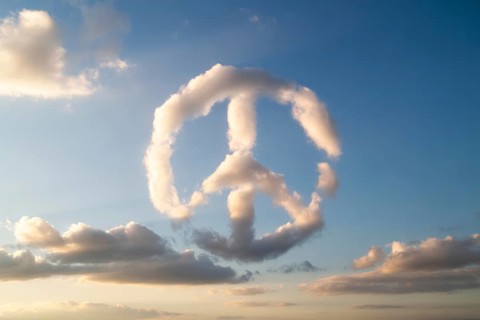 A naturally formed peace sign made of white clouds floats in a clear blue sky, symbolizing harmony