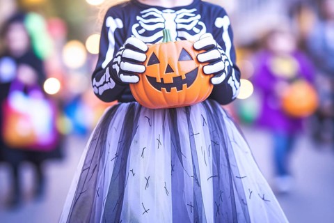 Girl child in skeleton costume with tulle skirt holding pumpkin candy bucket. Concept of Halloween