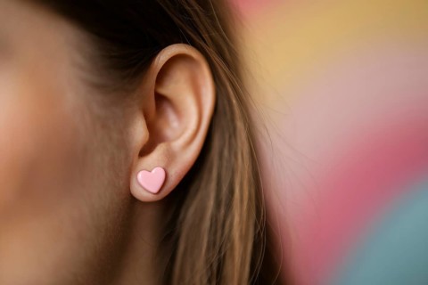 Close-up of pink heart-shaped earrings on woman's ear with soft pastel background. Generative Ai,