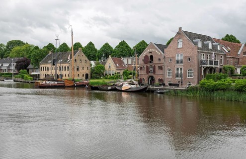 Tranquil river landscape with boats and brick buildings under a cloudy sky, Dokkum, Friesland,