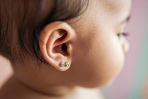 Two delicate diamond stud earrings in baby's ears bathed in warm golden light. Tender moment with
