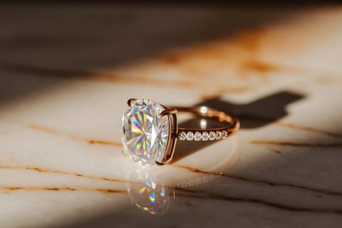 Close-up of diamond ring on polished marble surface with warm light and shimmering brilliance.