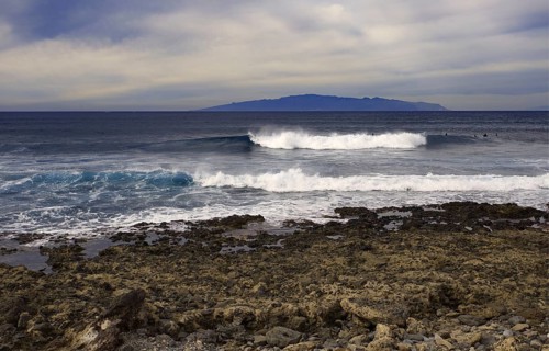 Coast with turbulent waves in front of a distant island (La Gomera) on the horizon, Tenerife,