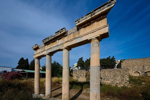 Three ancient columns with a fragment of the entablature, surrounded by ruins and blue sky, Xysto