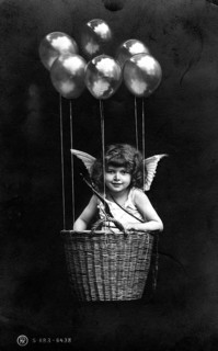 Cupid floating in basket with balloons, girl as angel in basket with balloons and wings,