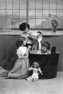 1910 Child being bathed by children, Two children playing in a black bathtub with dolls, Historical