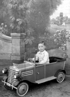 Little boy in car, 1930s, A boy sits in a toy car in front of a picturesque background, Historical