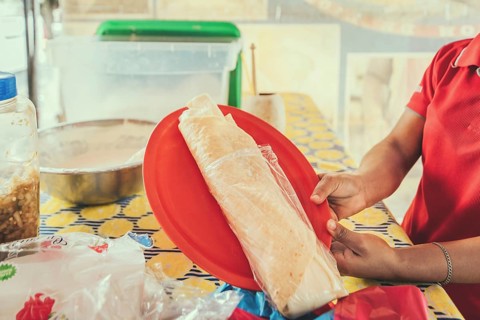 Hands of a person serving traditional quesillo. Vendor serving delicious quesillo in a bag