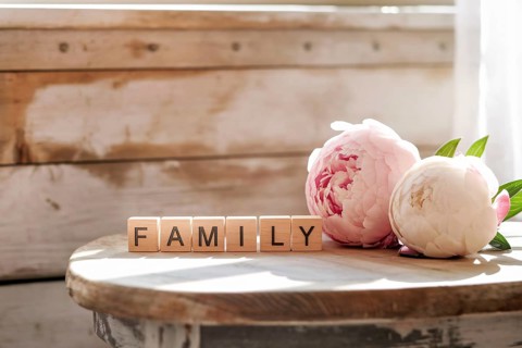 Wooden blocks spelling family beside peony flowers. A warm symbol of love, togetherness, and cozy