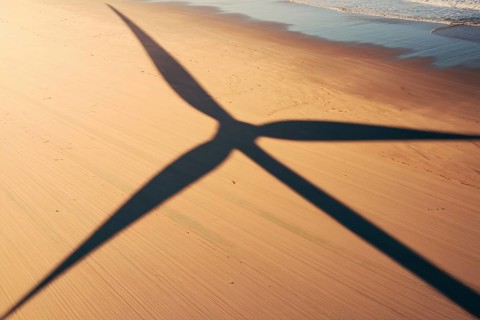 Wind turbine shadow on sunlit beach. A poetic symbol of clean energy blending with nature.