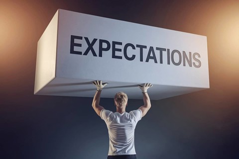 Man straining under block labeled expectations with work gloves, symbolizing male gender roles and