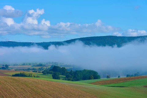 Fog moves through hilly landscape with blue sky, Mönchberg, Miltenberg, Spessart, Bavaria, Germany