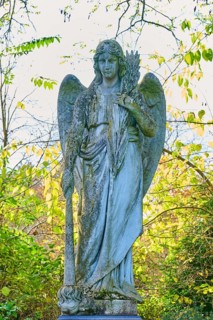 Angel made of stone with sword in an autumnal setting, surrounded by colourful leaves, cemetery,