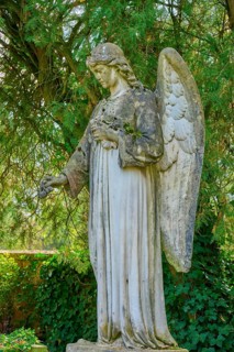 Stone angel in a green garden, surrounded by trees, atmosphere is quiet and peaceful, cemetery,